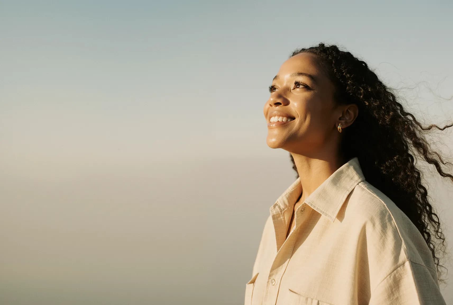 A smiling woman looking up at the sky in warm evening light